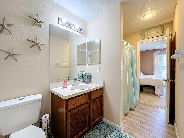 bathroom featuring baseboards, toilet, wood finished floors, a textured ceiling, and vanity