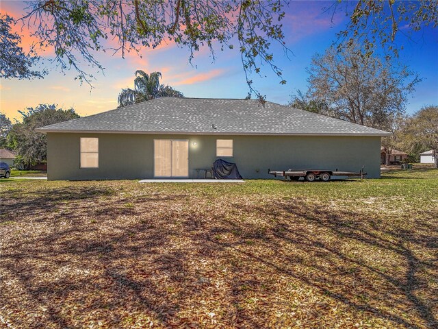 back of property at dusk featuring a lawn and stucco siding