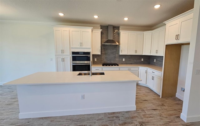 kitchen with a center island with sink, backsplash, stainless steel double oven, wall chimney range hood, and a sink