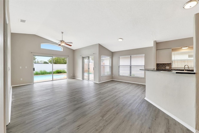 unfurnished living room with vaulted ceiling, wood finished floors, a sink, and a ceiling fan