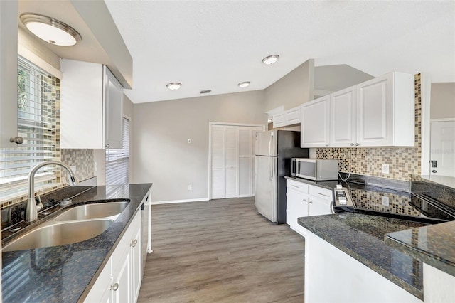 kitchen featuring vaulted ceiling, appliances with stainless steel finishes, dark stone counters, and a sink