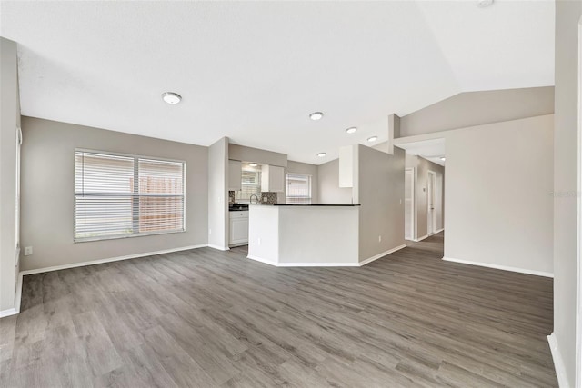 unfurnished living room with vaulted ceiling, wood finished floors, and baseboards