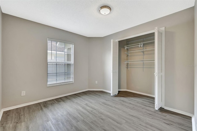 unfurnished bedroom with a textured ceiling, a closet, wood finished floors, and baseboards