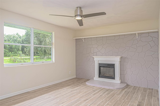 unfurnished living room featuring light wood-style flooring, baseboards, ceiling fan, and a glass covered fireplace