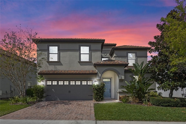 mediterranean / spanish-style home featuring a garage, a tiled roof, decorative driveway, and stucco siding