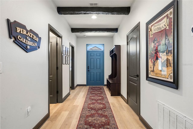 doorway to outside with light wood-type flooring, baseboards, visible vents, and beam ceiling