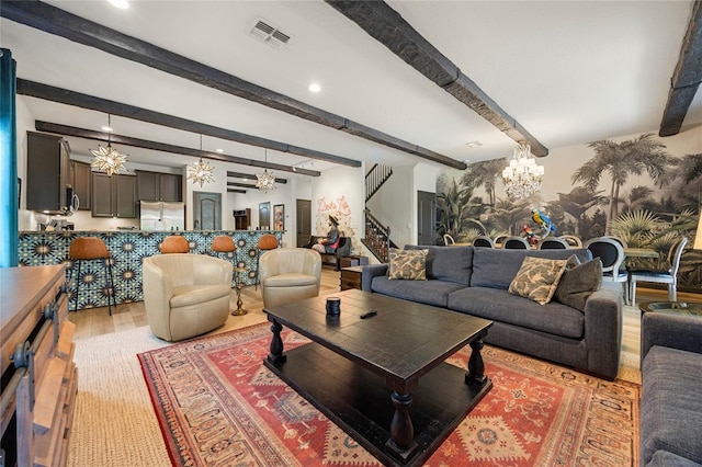 living area featuring beam ceiling, a notable chandelier, light wood finished floors, visible vents, and stairs