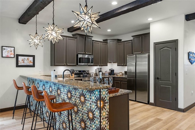 kitchen with dark stone counters, light wood-style flooring, appliances with stainless steel finishes, beamed ceiling, and a peninsula