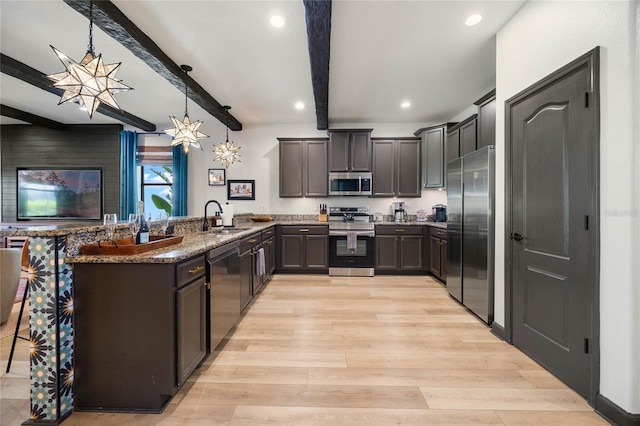 kitchen with a peninsula, a sink, light wood-style floors, appliances with stainless steel finishes, and dark stone counters