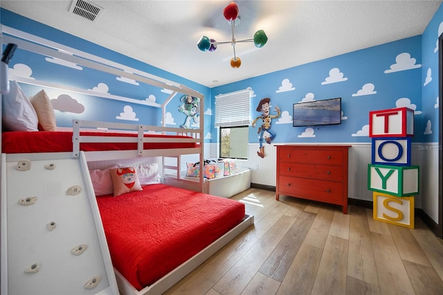 bedroom featuring light wood-type flooring, wainscoting, visible vents, and a textured ceiling