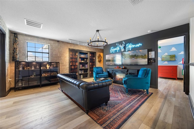 living area with wood-type flooring, visible vents, a notable chandelier, and a textured ceiling