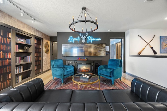 living room with a textured ceiling, wood finished floors, a glass covered fireplace, and a chandelier