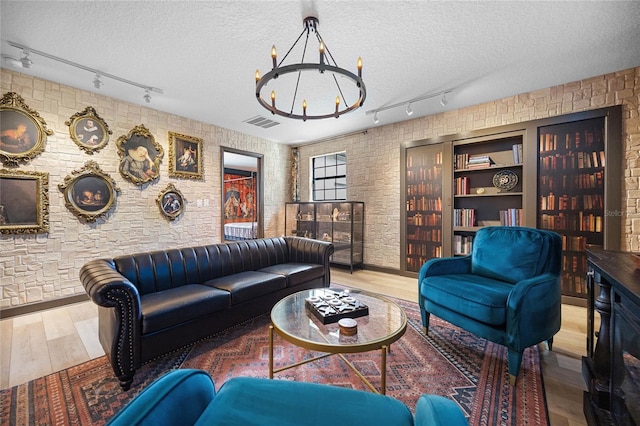 living room featuring a textured ceiling, a chandelier, wood finished floors, visible vents, and track lighting