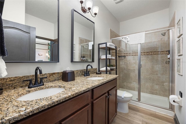 bathroom with double vanity, a stall shower, a sink, and wood finished floors