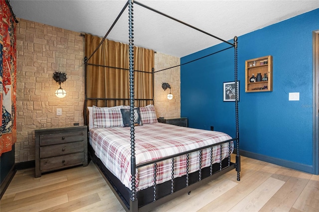 bedroom with a textured ceiling, brick wall, baseboards, and light wood-style floors