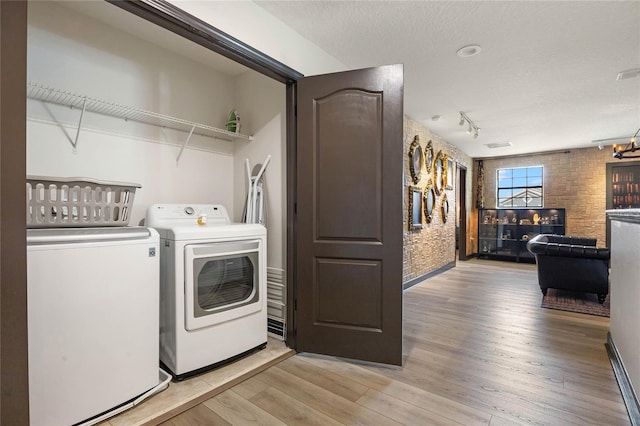 clothes washing area with light wood-style floors, washing machine and dryer, track lighting, brick wall, and laundry area