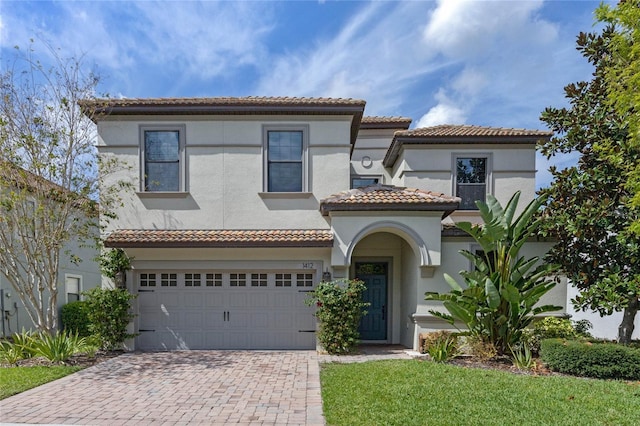 mediterranean / spanish-style house with a garage, decorative driveway, a tile roof, and stucco siding