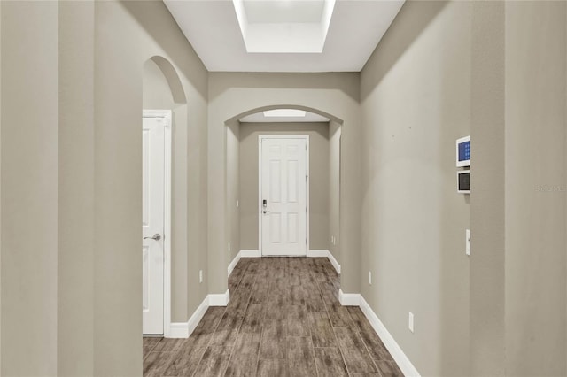 hall with arched walkways, a tray ceiling, baseboards, and wood finished floors