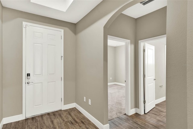 entryway featuring wood finish floors, baseboards, arched walkways, and visible vents