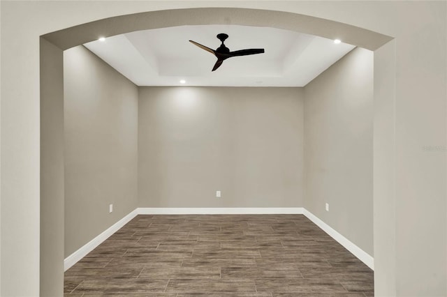 unfurnished room featuring a raised ceiling, wood finished floors, a ceiling fan, and baseboards