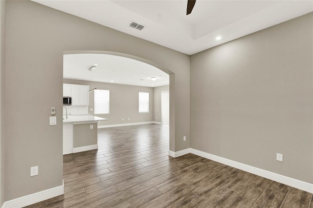 unfurnished room featuring visible vents, a ceiling fan, arched walkways, baseboards, and dark wood-style flooring