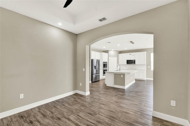 unfurnished living room featuring arched walkways, visible vents, wood finished floors, and a sink