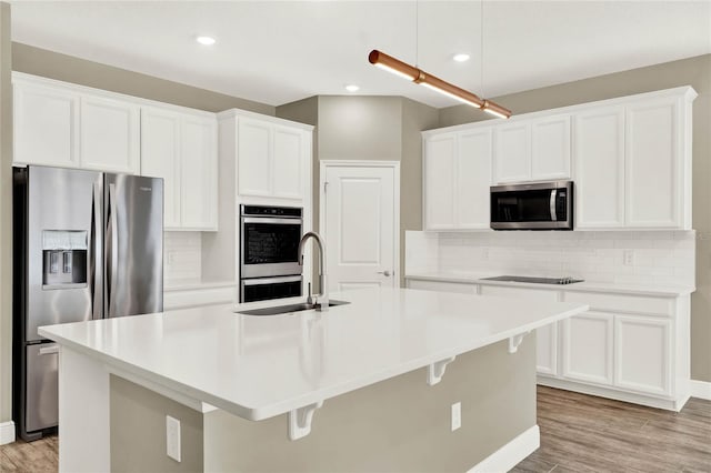 kitchen with a center island with sink, decorative backsplash, appliances with stainless steel finishes, white cabinetry, and a sink