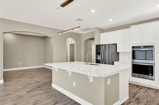 kitchen featuring an island with sink, a sink, light countertops, light wood-style floors, and appliances with stainless steel finishes