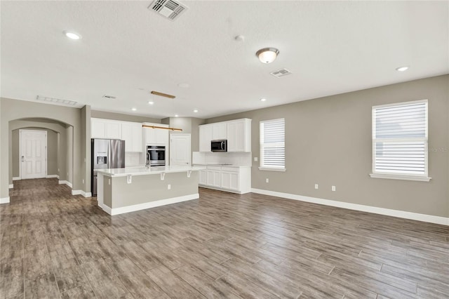 unfurnished living room with wood finished floors, arched walkways, visible vents, and baseboards