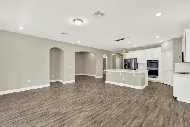 unfurnished living room featuring wood finished floors, recessed lighting, arched walkways, and visible vents