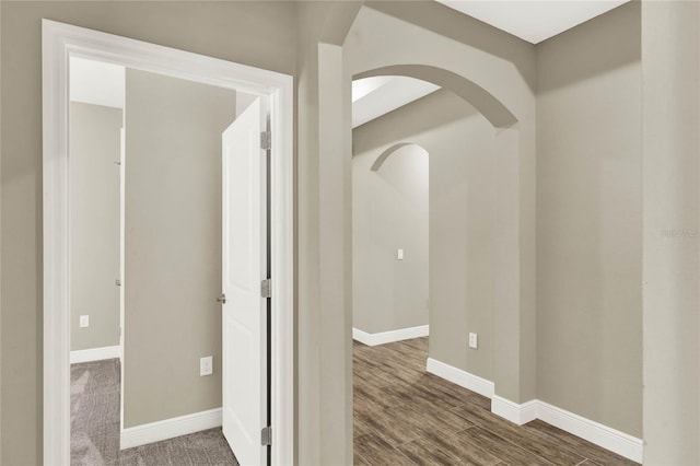 hall featuring baseboards, arched walkways, and wood finished floors