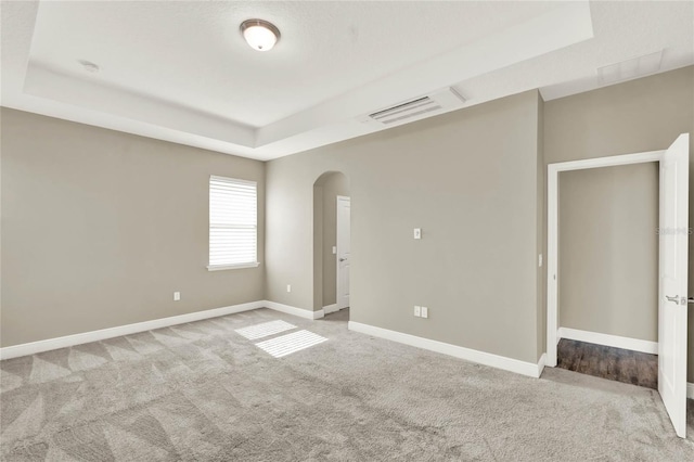 carpeted empty room featuring arched walkways, visible vents, baseboards, and a tray ceiling