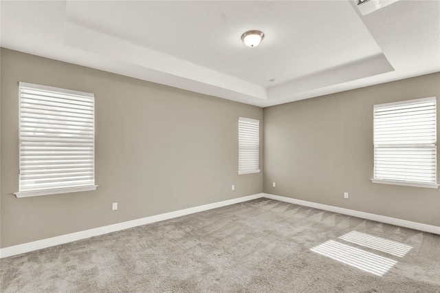 carpeted empty room featuring a raised ceiling and baseboards