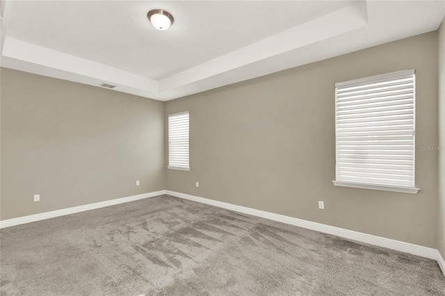 carpeted spare room with a tray ceiling, visible vents, and baseboards