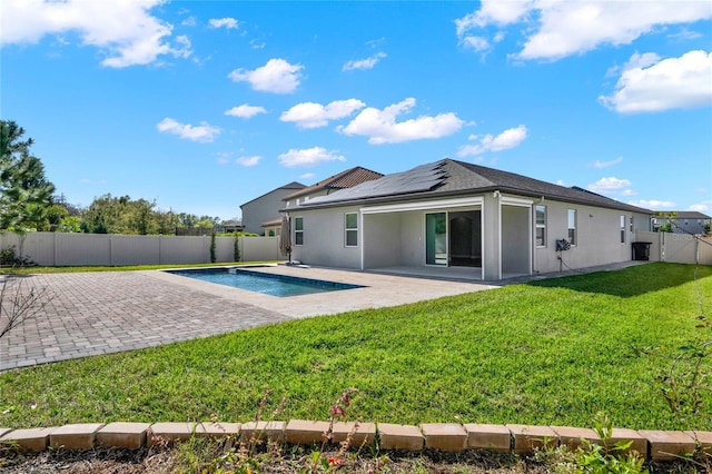 rear view of property with roof mounted solar panels, stucco siding, a yard, a fenced backyard, and a patio