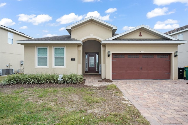 ranch-style home with a garage, central air condition unit, decorative driveway, and stucco siding