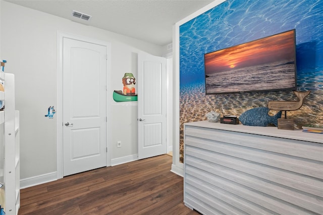 interior space featuring a textured ceiling, dark wood-type flooring, visible vents, and baseboards