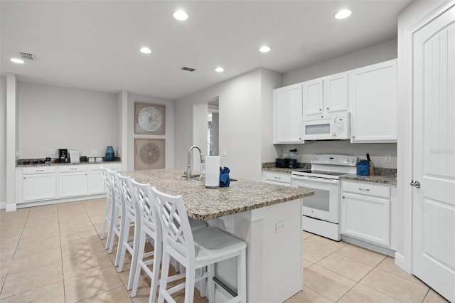 kitchen featuring light tile patterned floors, recessed lighting, visible vents, a kitchen island with sink, and white appliances