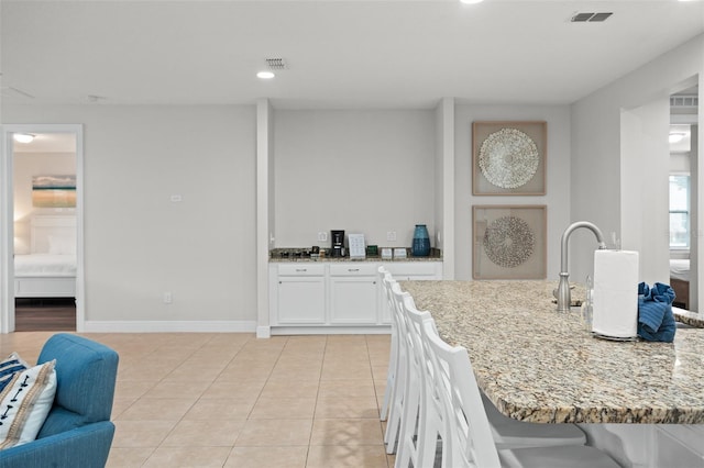 kitchen with light stone counters, light tile patterned floors, visible vents, white cabinets, and baseboards