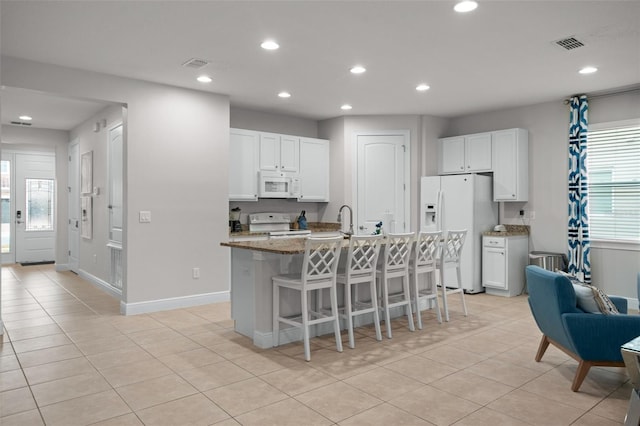 kitchen with white appliances, an island with sink, a breakfast bar, and visible vents