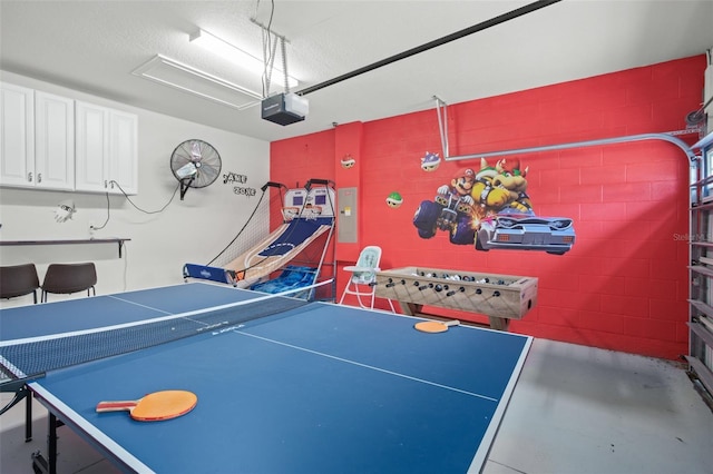 recreation room with a textured ceiling, a garage, concrete floors, electric panel, and concrete block wall