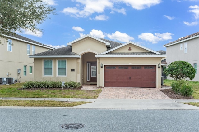 ranch-style house with a garage, roof with shingles, decorative driveway, and stucco siding