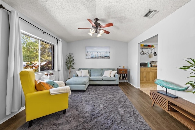 living area featuring visible vents, a ceiling fan, a textured ceiling, wood finished floors, and vaulted ceiling