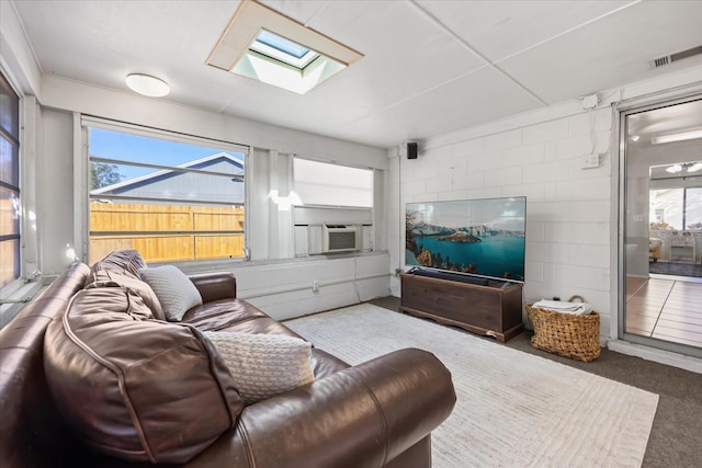 carpeted living area with visible vents, cooling unit, a skylight, and concrete block wall