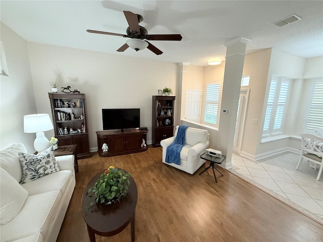 living area featuring wood finished floors, baseboards, visible vents, decorative columns, and ceiling fan