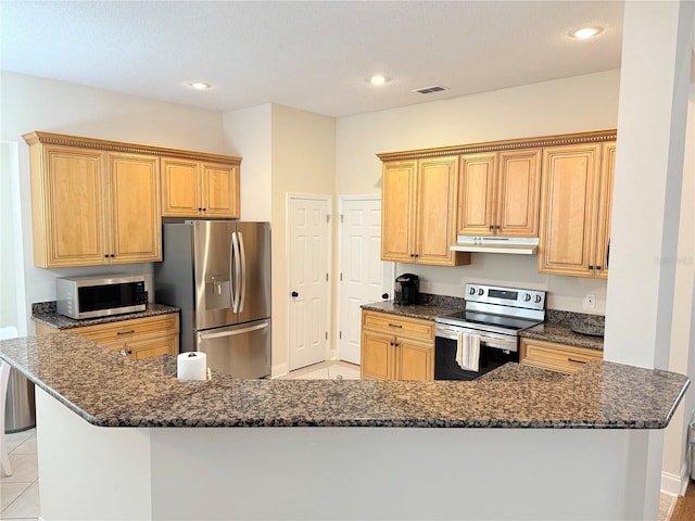 kitchen with visible vents, under cabinet range hood, dark stone countertops, appliances with stainless steel finishes, and light tile patterned flooring