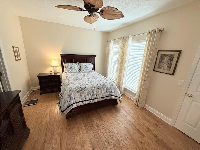 bedroom with ceiling fan, baseboards, light wood finished floors, and a textured ceiling