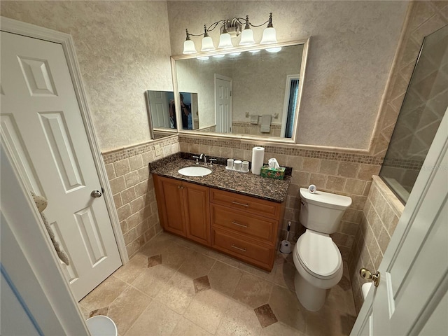 bathroom with tile walls, toilet, a tile shower, wainscoting, and vanity