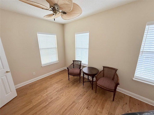 living area with plenty of natural light, light wood-style floors, baseboards, and ceiling fan