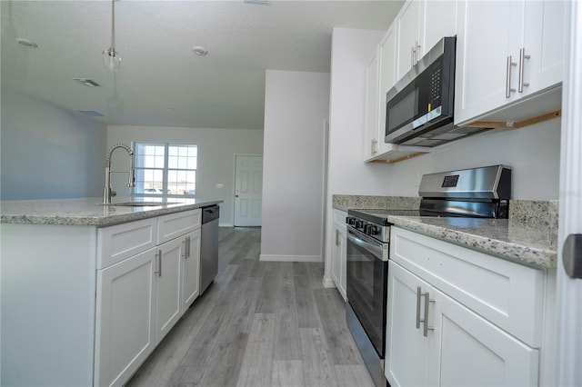 kitchen with light wood finished floors, stainless steel appliances, white cabinetry, a sink, and light stone countertops